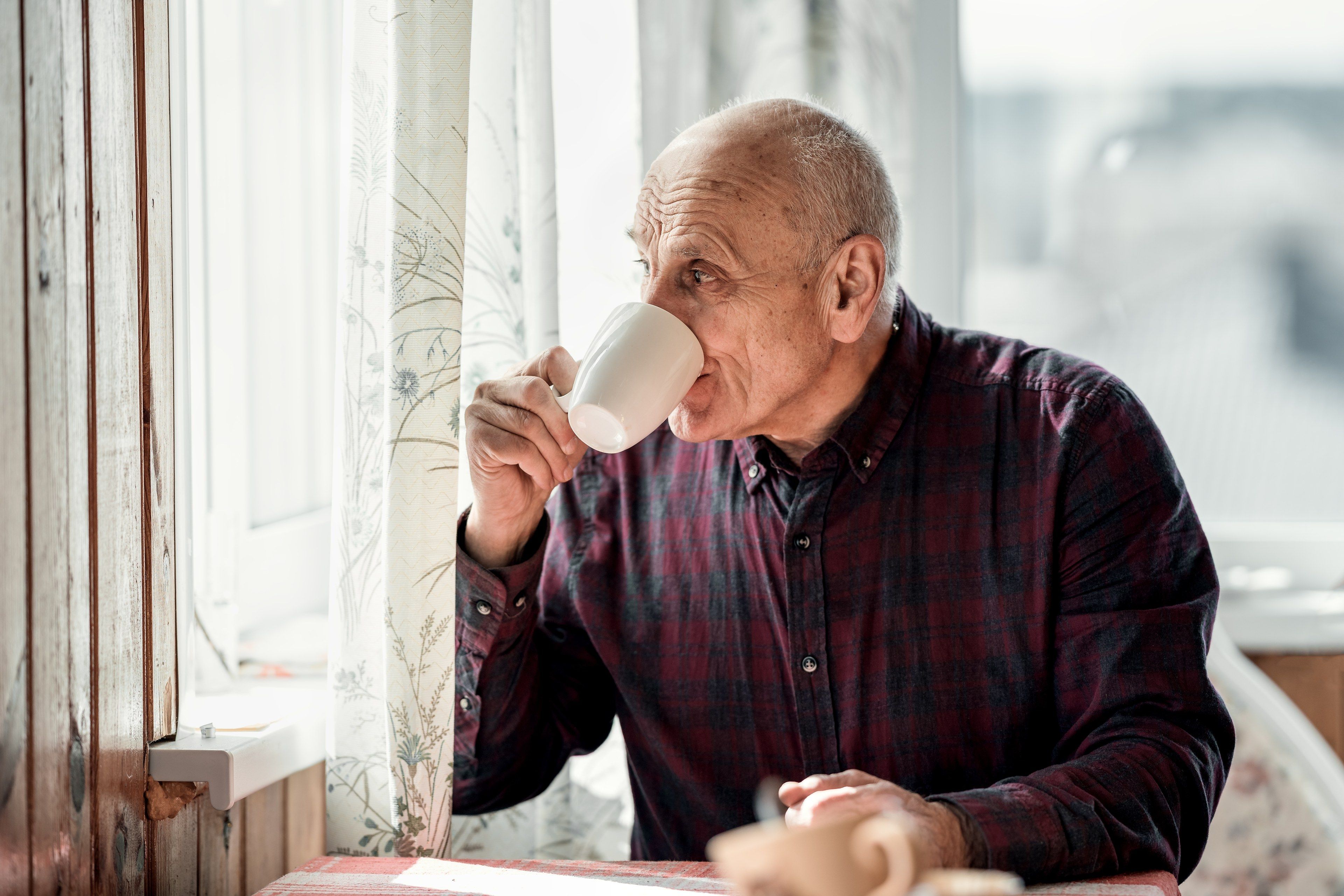 Eldre mann drikker kaffe ved vinduet hjemme