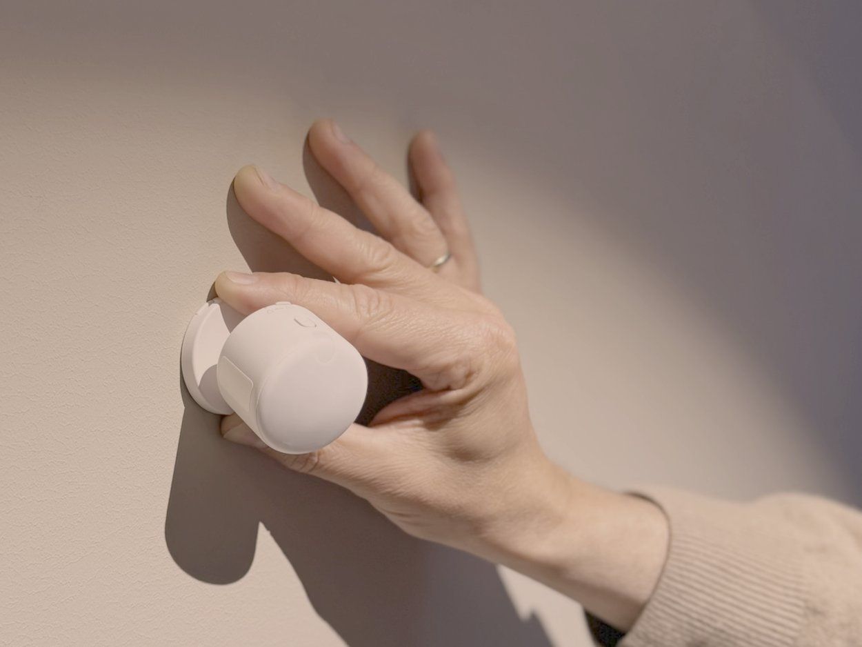 En hånd fester en liten, hvit sensor på veggen
