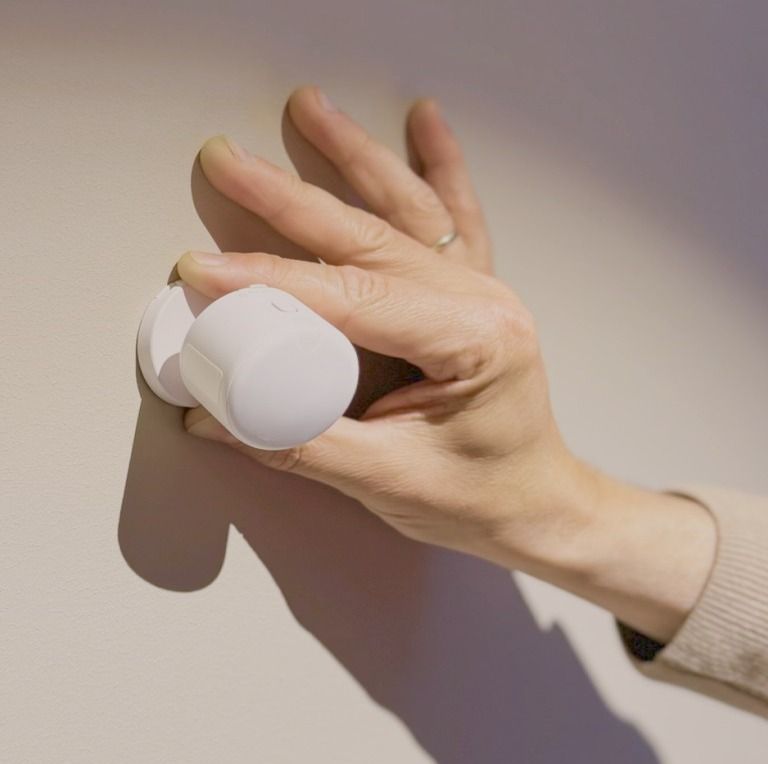 En hånd fester en liten, hvit sensor på veggen